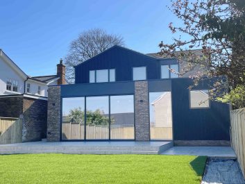 Rear view of a fully refurbished house in Saffron Walden with modern extension, featuring black cladding, large sliding glass doors, and yellow brick detailing near a conservation area.